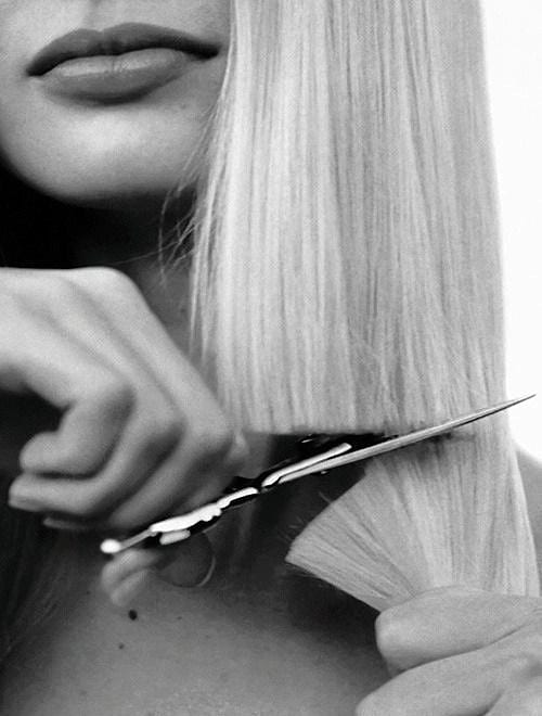 Black and white close-up of scissors cutting blonde hair near a person's lips